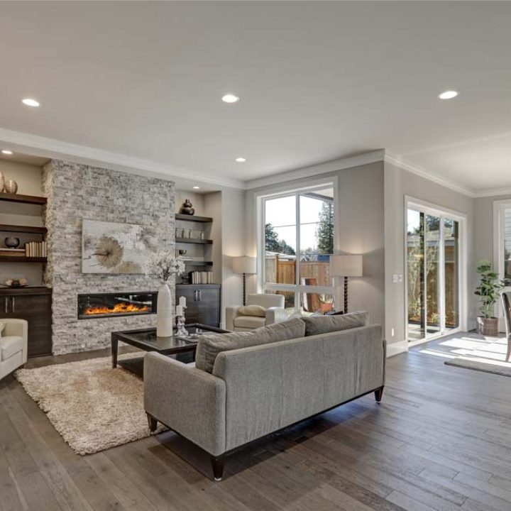 Living room interior in gray and brown colors features gray sofa atop dark hardwood floors facing stone fireplace with built-in shelves