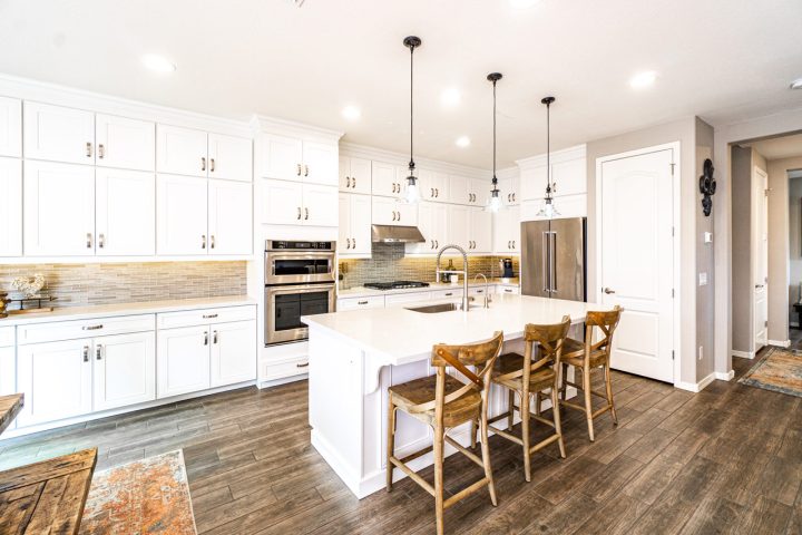 a modern kitchen with white cabinets, backsplash, an island with three chairs