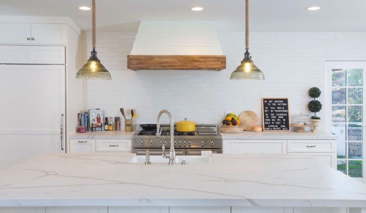 a kitchen newly remodelled, white painted cabinet, white kitchen backsplash, marble counter top, gas range and a center island with sink